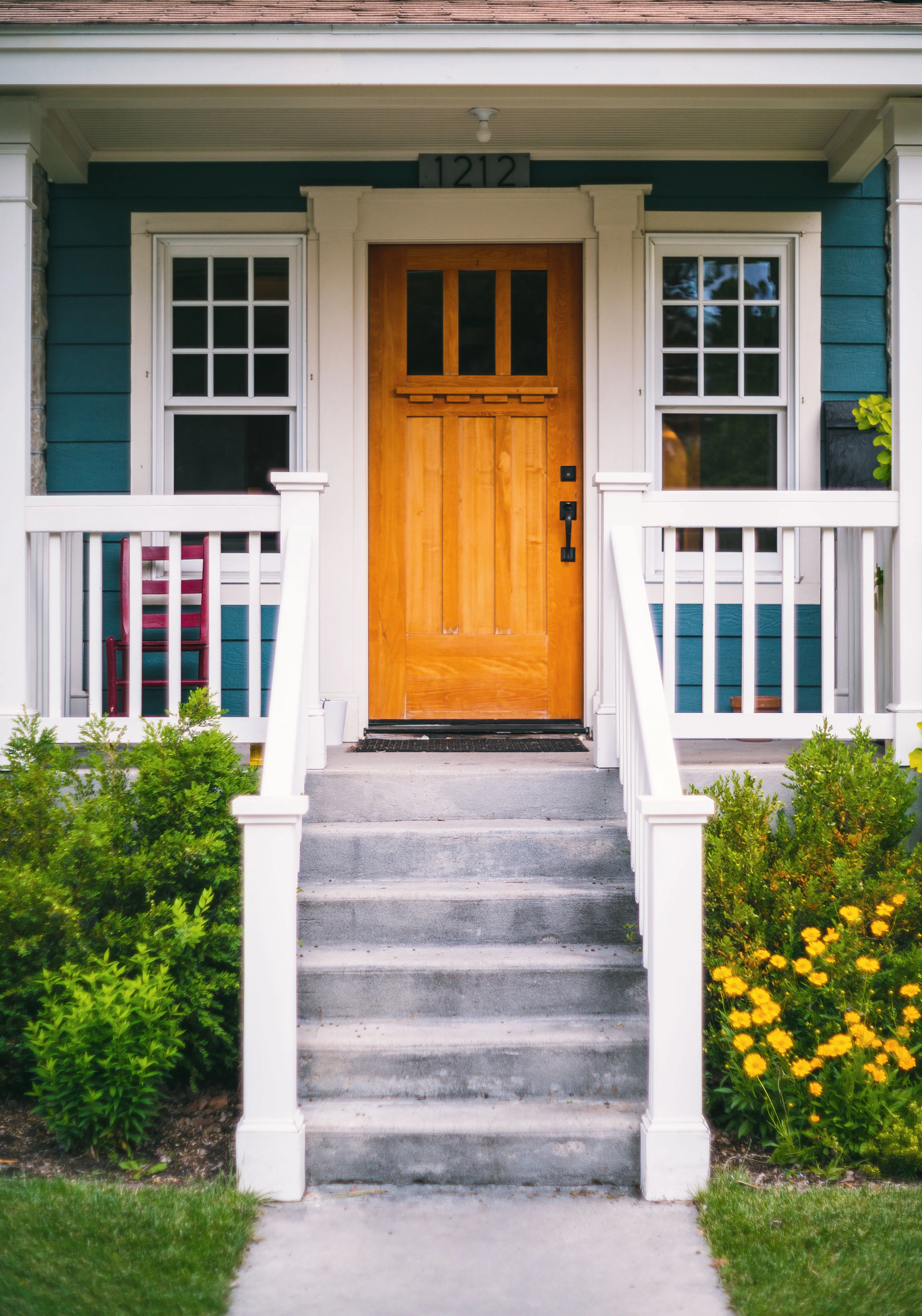 A wood front door with a white porch rail and steps, flowers along the path