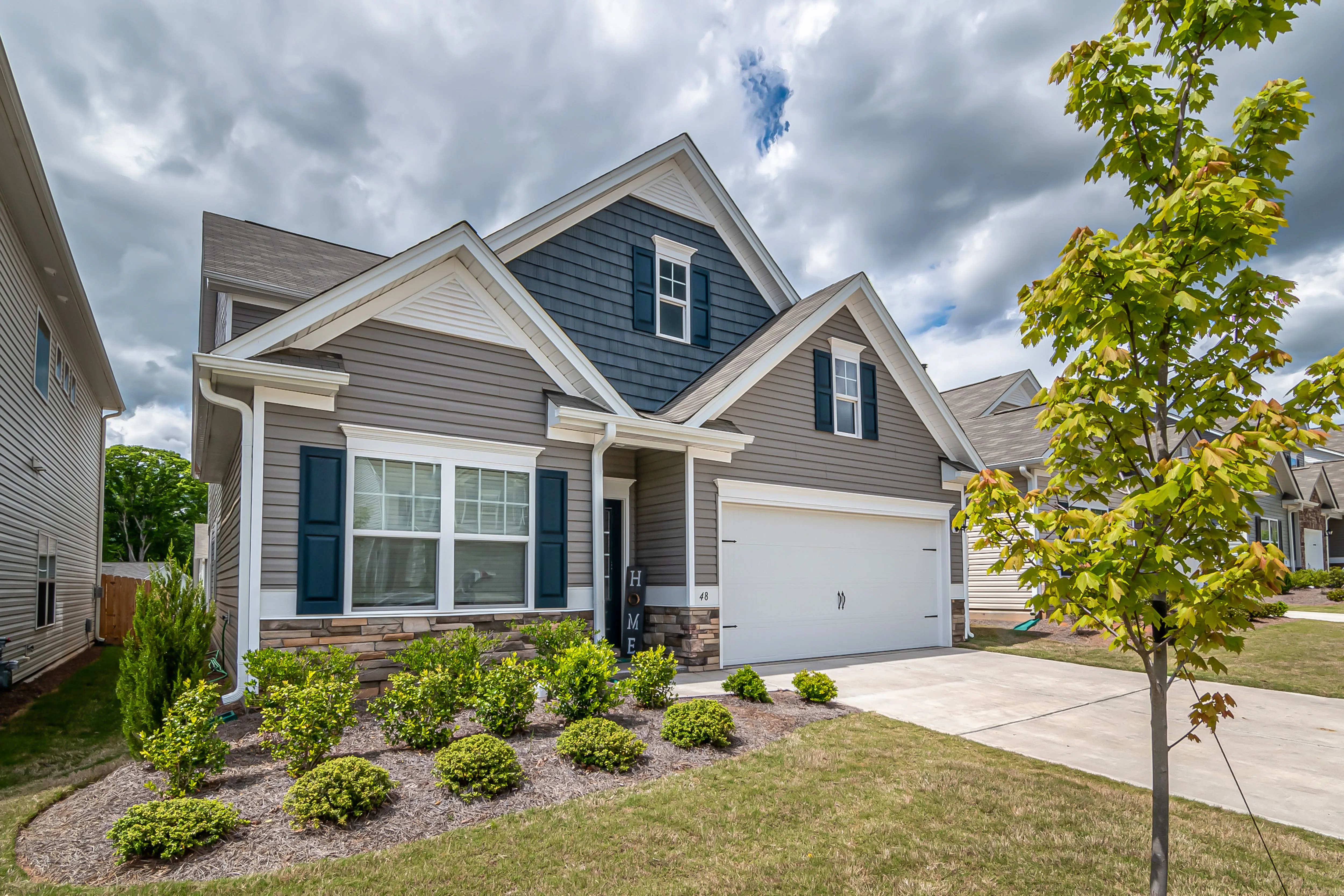 A grey two-storey home with white trim, a manicured front garden and a double garage under a cloudy sky