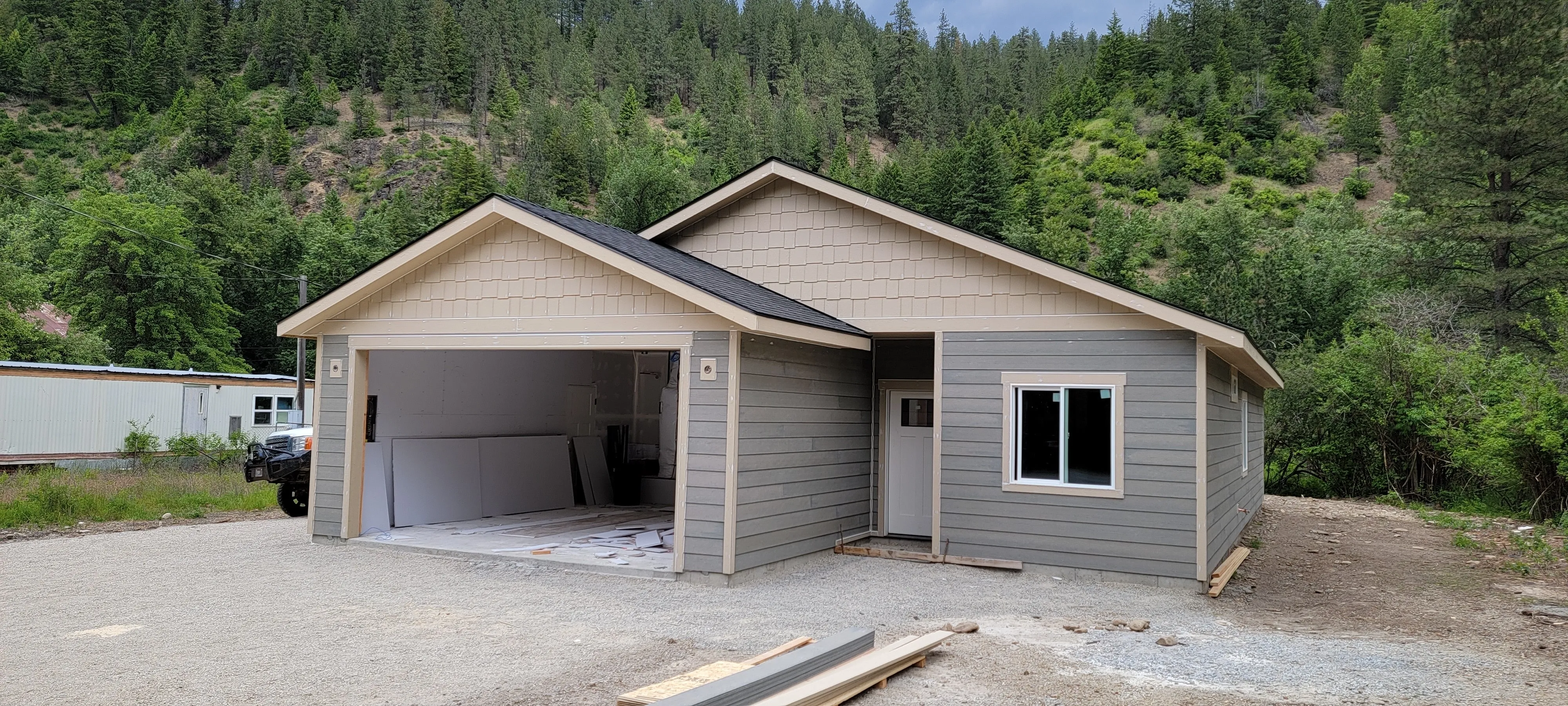 One of Jared's finished builds: a single-storey home with grey siding and a double garage, a forested hillside behind it