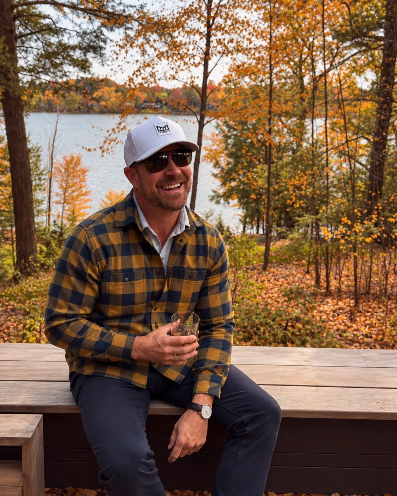 Jared Ban on a deck in a plaid flannel shirt, smiling, autumn timber behind him