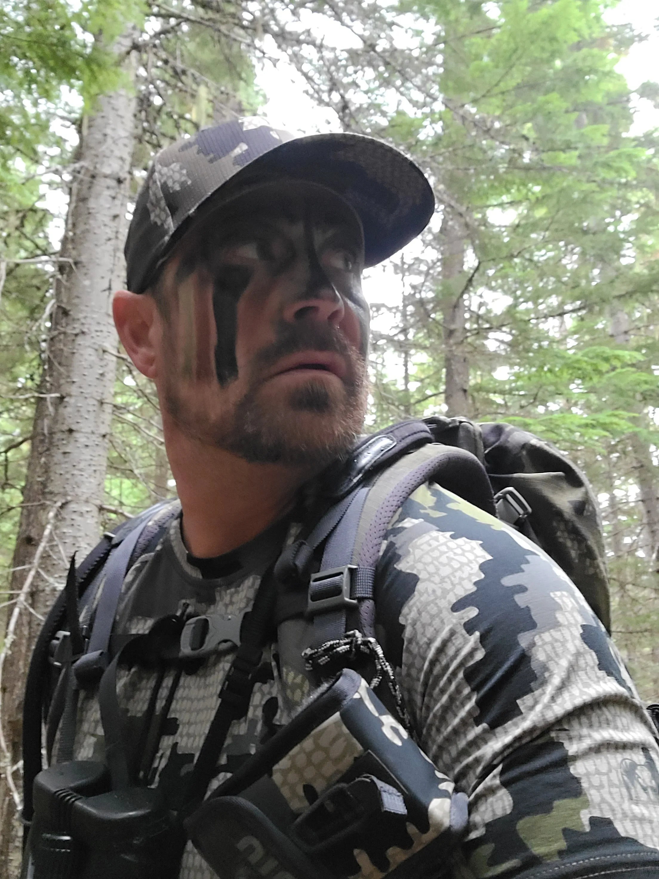 Jared Ban in camouflage and face paint in the timber on a hunt, a pack strapped over his shoulders