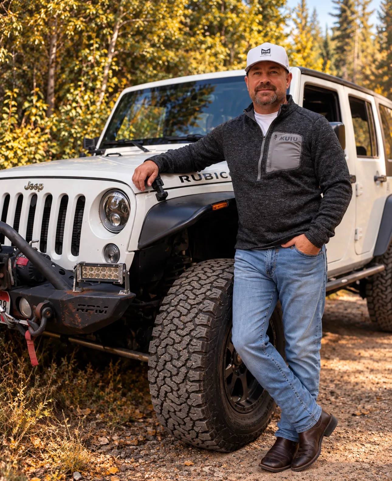 Jared Ban leaning against the front of his white Jeep, arms folded, timber behind him