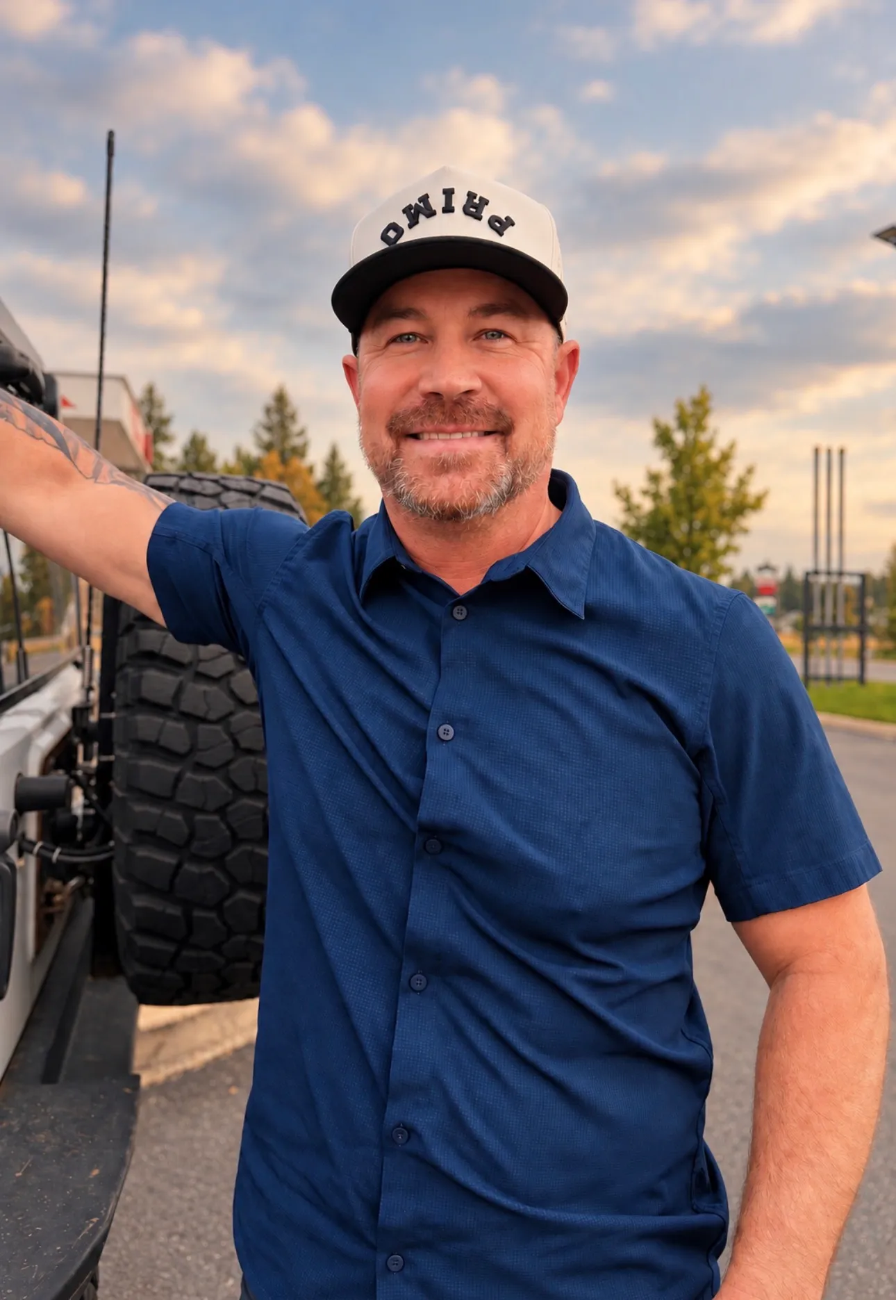 Jared Ban standing beside his Jeep in a blue shirt, smiling, timber and open sky behind him