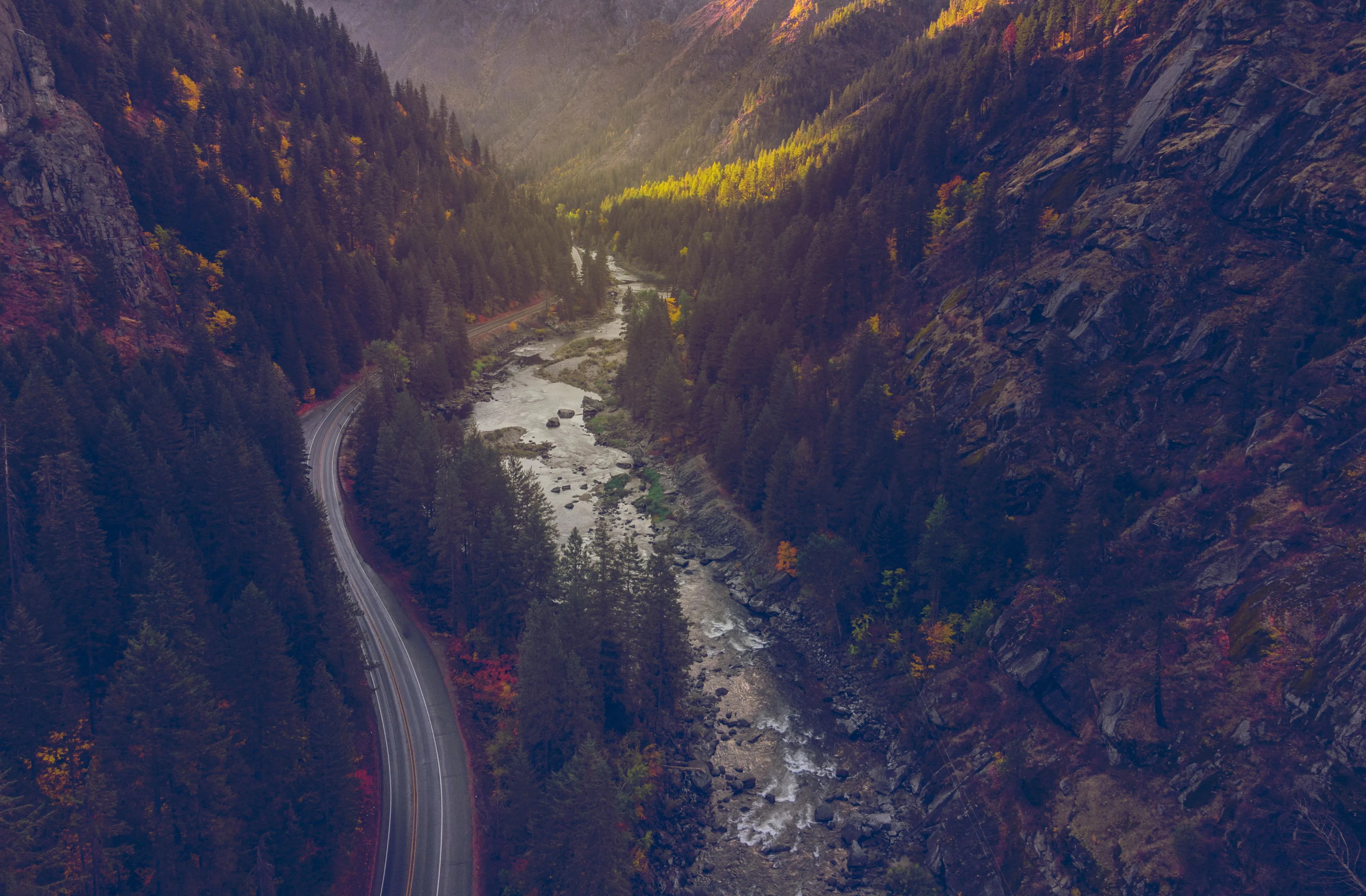 An aerial view of a river winding through a steep forested canyon in autumn colour, a road tracing the far bank
