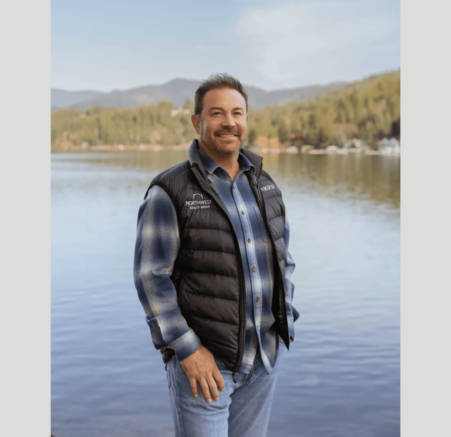 Man smiling by a lake with mountains.