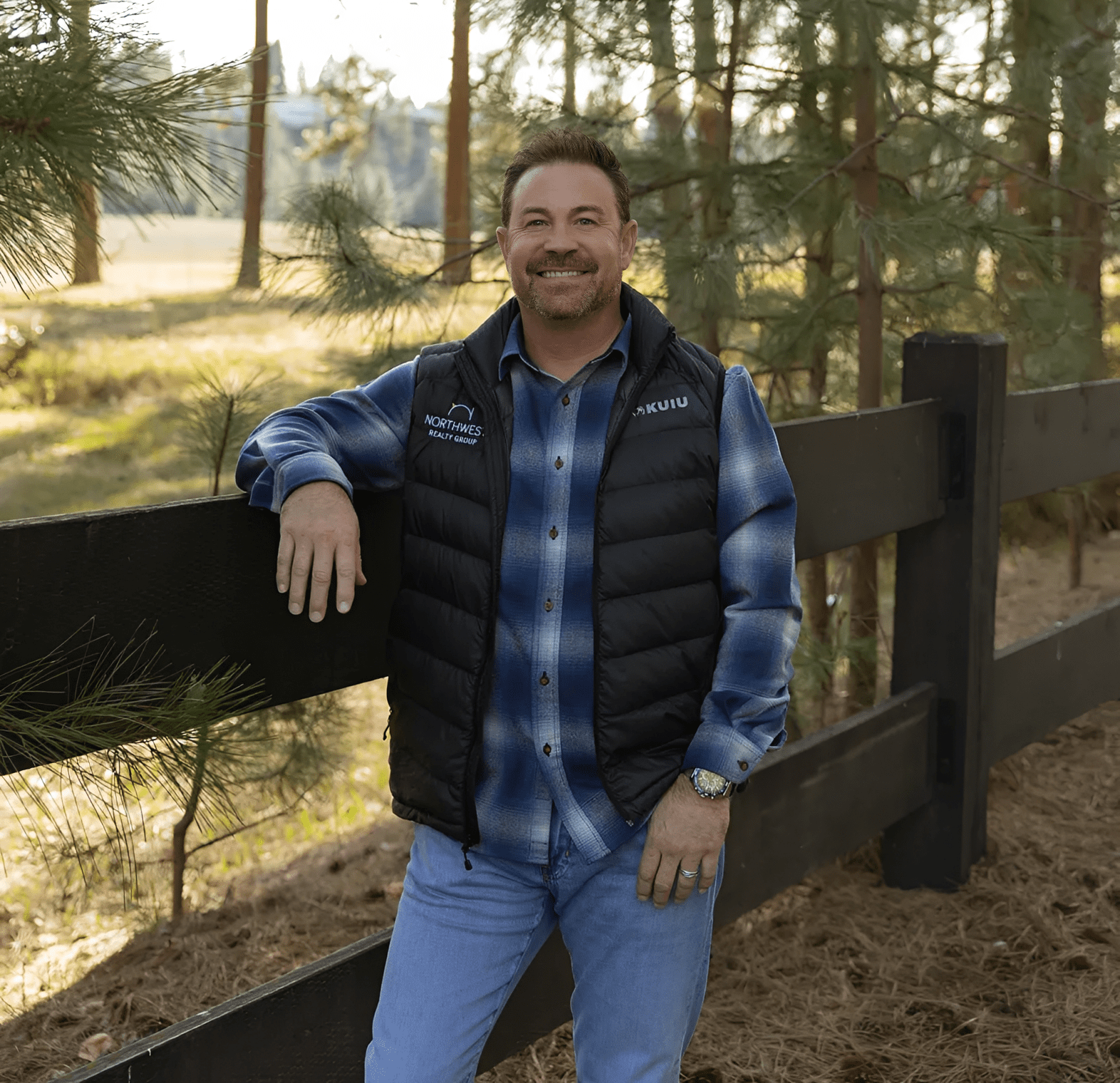 Man leaning on wooden fence in forest.